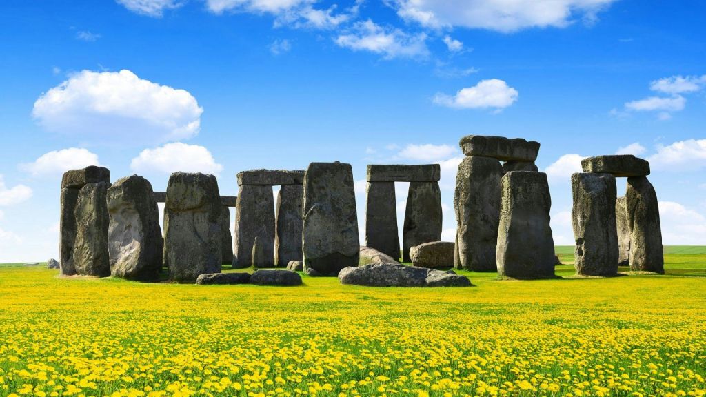 스톤헨지 스톤 서클은 부분적으로 흐린 푸른 하늘 아래 노란 꽃밭으로 둘러싸여 있습니다.