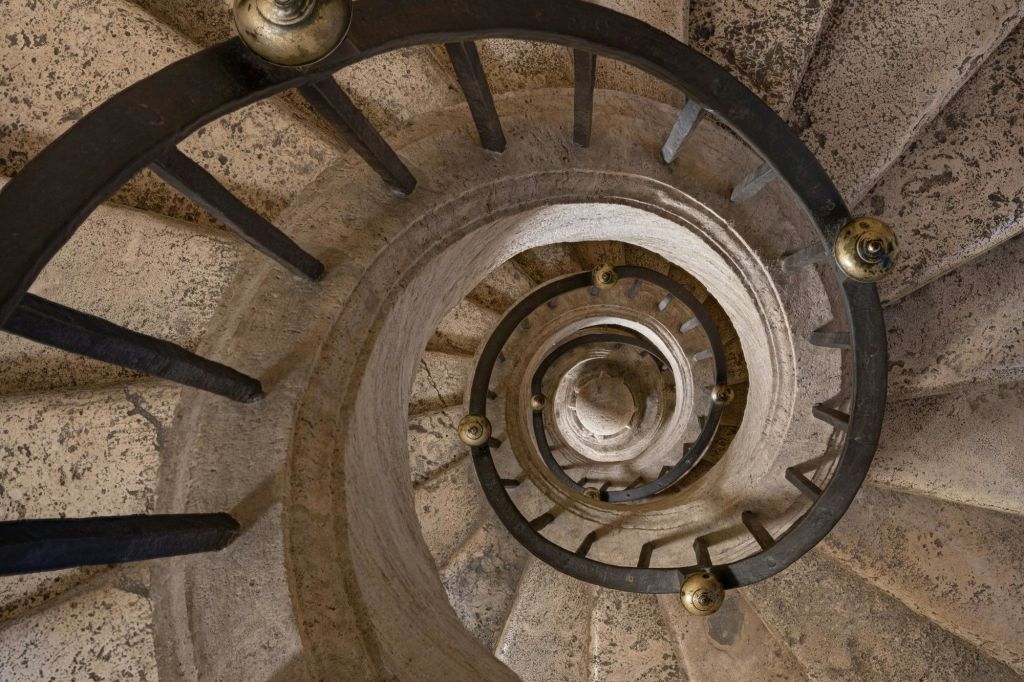 위에서 바라본 검은 금속 난간이 있는 나선형 돌 계단은 여러 개의 하강 층을 보여줍니다.