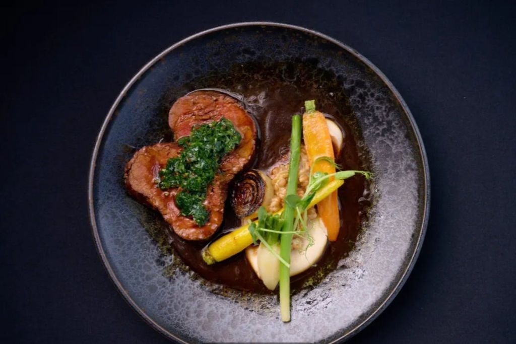 진한 접시에 그린 소스, 야채, 으깬 감자를 얹어 고기를 썰어 놓은 고급 요리입니다.