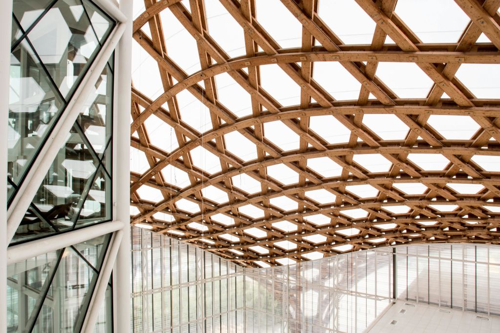 커다란 나무 격자 천장 구조와 유리 벽이 있는 현대적인 건물 내부.