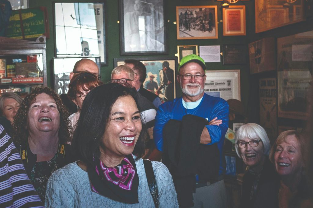 짙은 녹색 벽에 액자 그림과 기념품이 놓인 방에서 한 무리의 사람들이 웃고 있습니다.