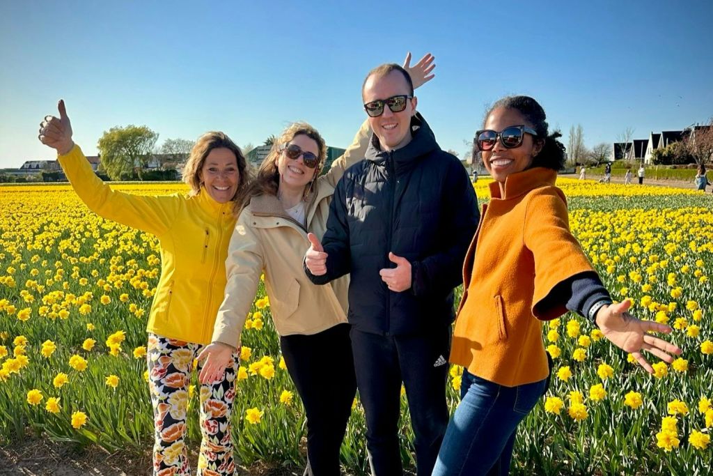 맑고 푸른 하늘 아래 노란 꽃밭에서 웃으며 포즈를 취하는 네 사람.