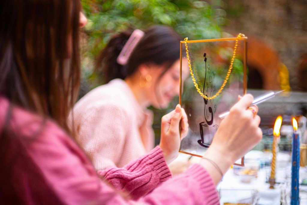 두 사람이 테이블에 앉아 있는데, 하나는 황금색 체인이 달린 투명한 프레임과 그 위에 추상적인 디자인을 들고 있습니다.