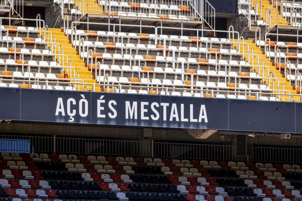 주황색, 빨간색 및 흰색 음영으로 표시된 빈 경기장 좌석 앞에 "ACÒ ÉS MESTALLA" 라고 적힌 표지판이 있습니다.