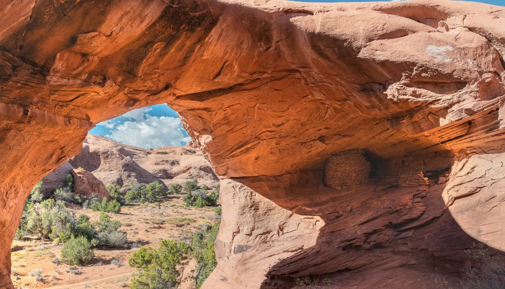 나무와 수풀이 우거진 사막 풍경과 구름이 우거진 푸른 하늘을 형상화한 붉은 바위 아치입니다.