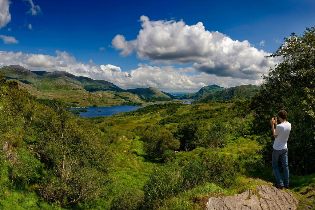 부분적으로 흐린 푸른 하늘 아래 언덕으로 둘러싸인 호수가 있는 울창한 푸른 계곡의 경치.