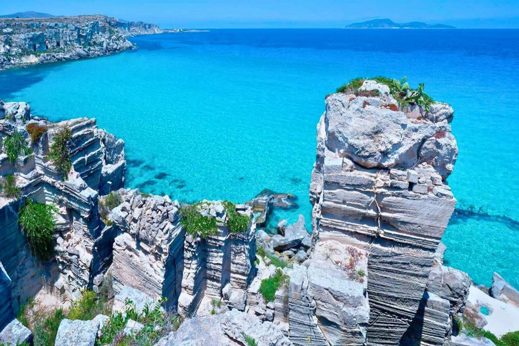 맑고 푸른 하늘 아래 전경에 험준한 암석이 있는 청록색 바다.