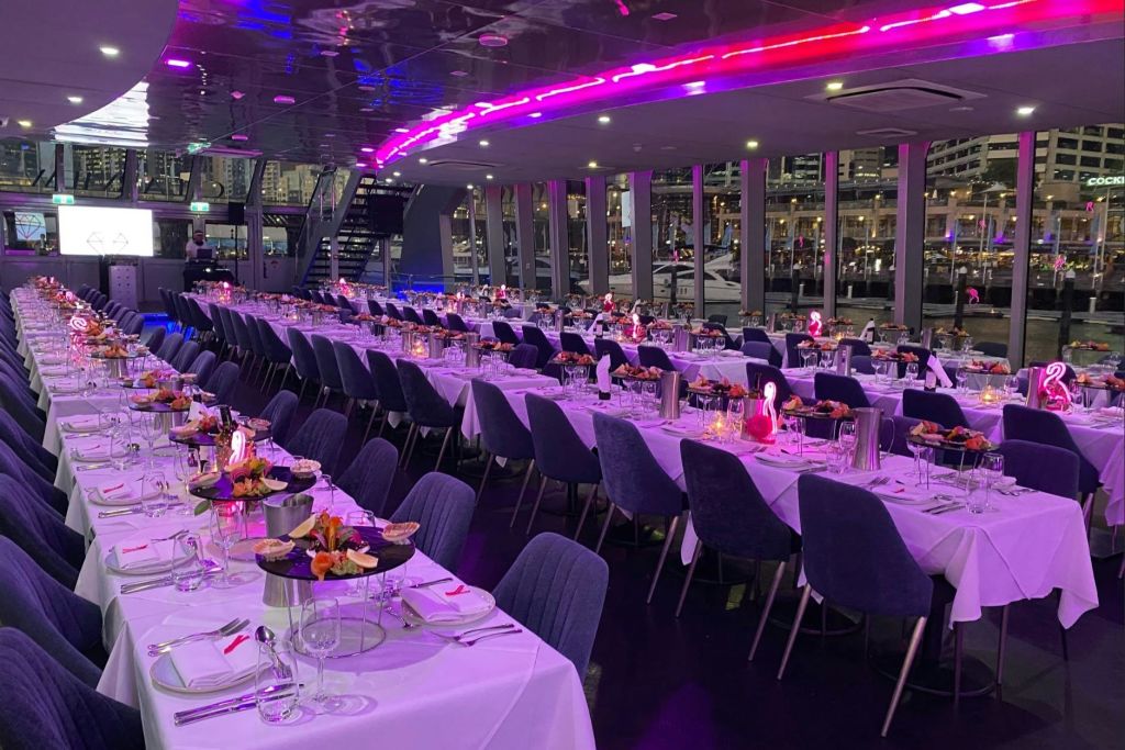 현대적인 공간에 접시와 꽃으로 장식된 흰색 천으로 덮인 테이블이 줄지어 있는 우아한 연회장입니다.