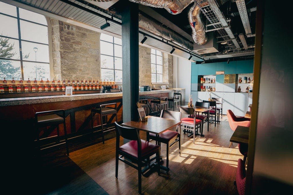 나무 테이블, 의자, 병이 놓인 바, 커다란 창문, 인더스트리얼 스타일의 인테리어가 돋보이는 현대적인 카페입니다.