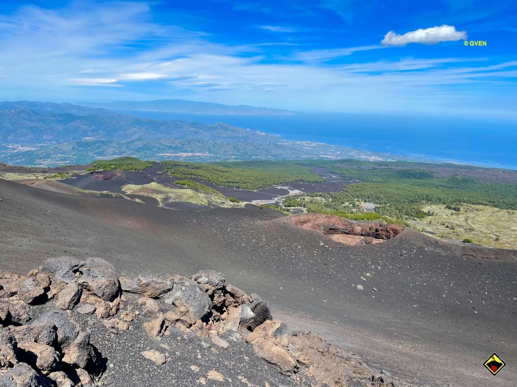 울창한 푸른 계곡, 구불구불한 도로, 밝고 푸른 하늘 아래 먼 해안선이 내려다보이는 화산 경사면에서 바라보는 풍경.