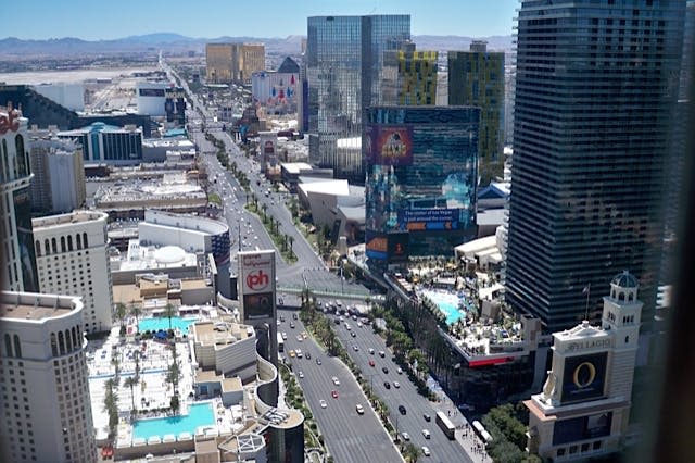 높은 건물과 광고판이 늘어선 번화한 도시 거리의 공중 전망, 수영장과 교통량이 많은 다차선 도로가 측면에 있습니다.