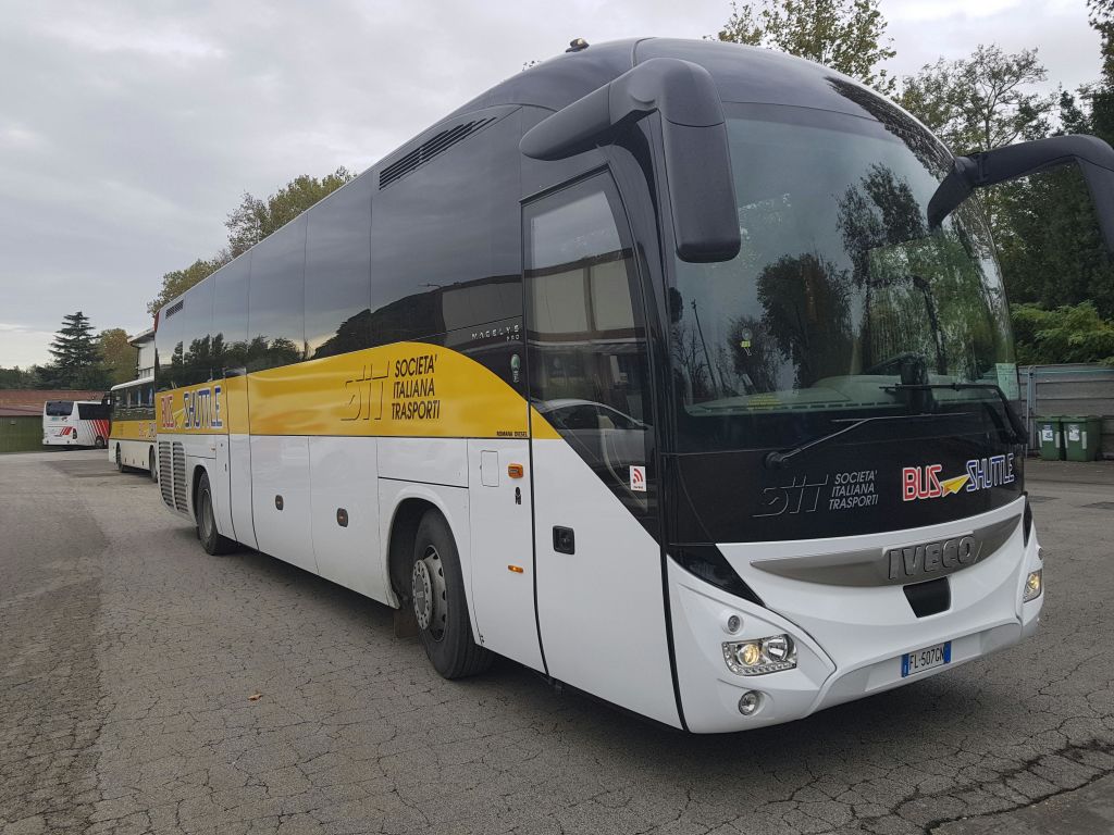 도로에 주차된 흰색과 노란색의 대형 버스는 "Società Italiana Trasporti" 라고 표시되어 있습니다. 나무가 배경으로 보입니다.
