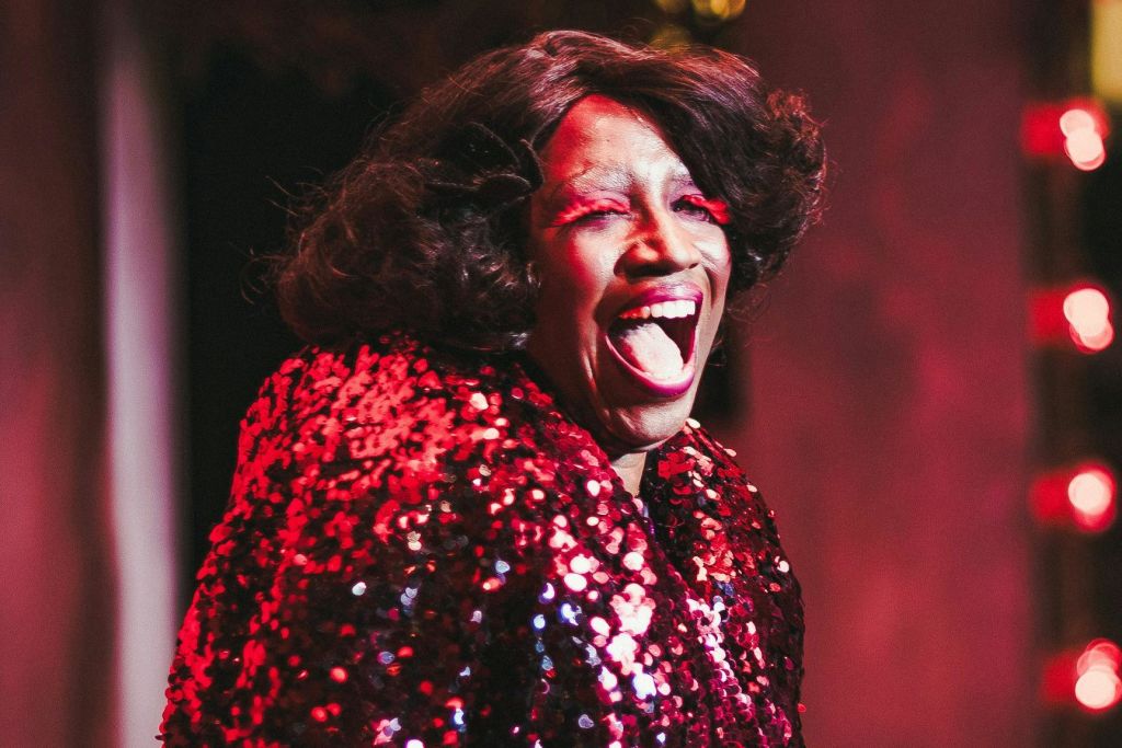 무대 조명 아래에서 활짝 웃고 있는 빨간색 의상을 입은 사람.