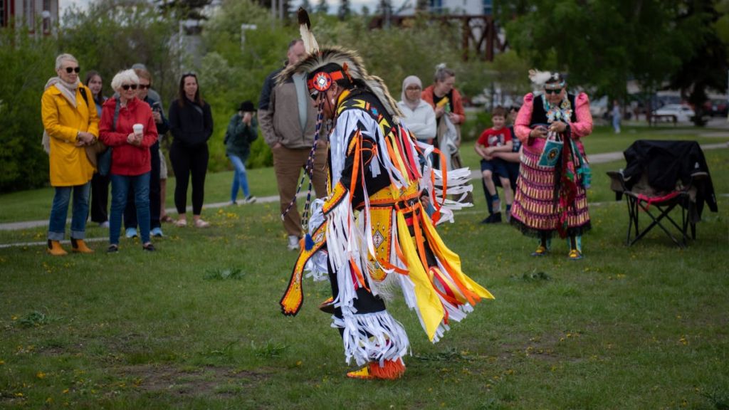 전통 레갈리아를 입은 사람이 야외에서 춤을 추는 동안 캐주얼 복장을 한 구경꾼이 여러 명 있습니다.