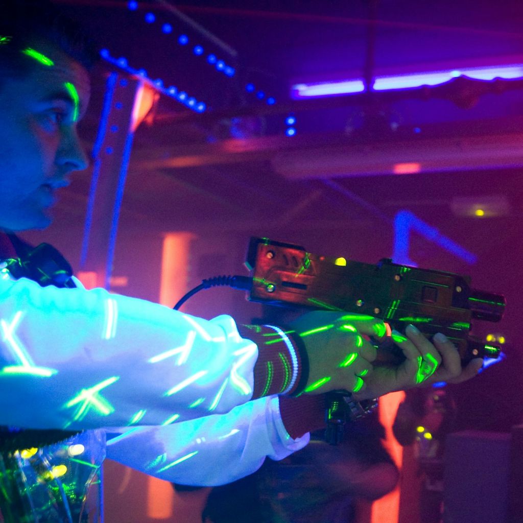 어두운 네온 조명 환경에서 레이저 태그 건을 들고 빛나는 디자인의 흰색 재킷을 입은 사람.