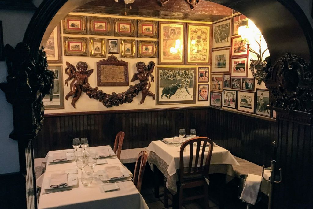 벽에 액자 그림과 예술품이 놓인 아늑한 레스토랑 코너로, 두 개의 테이블 위에 그룹 조각품으로 장식되어 있습니다.