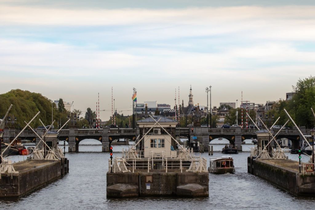부분적으로 흐린 하늘 아래 다리, 계류 구조물, 물속의 보트, 건물을 배경으로 한 운하 풍경.