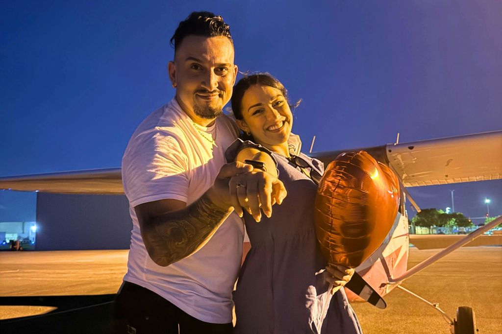 한 남녀가 미소를 지으며 카메라를 가리키고 있습니다. 여자는 하트 모양의 빨간 풍선을 들고 있습니다.