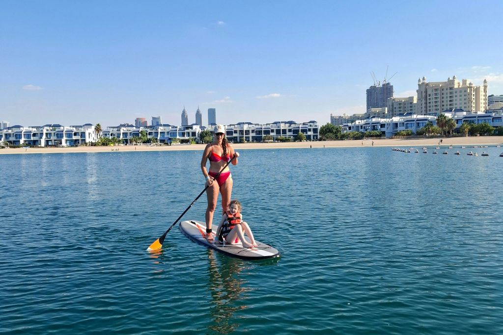 한 여성이 도시의 스카이라인을 배경으로 잔잔한 물줄기에 앉아 스탠드업 패들보드에 노를 젓고 있습니다.