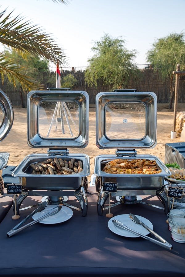 하나는 소시지, 다른 하나는 프리타타를 곁들인 두 가지 차핑 요리가 야외 환경에서 뷔페 테이블에 놓여 있습니다.