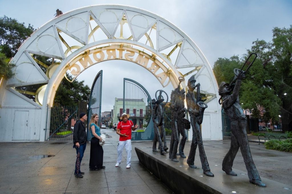 음악가 조각상 근처에 "암스트롱" 이라고 쓰여진 조명 아치형 통로 아래에 세 사람이 서 있습니다.