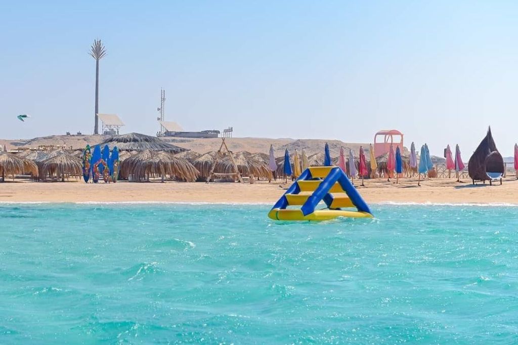 모래 해변과 초가 우산을 배경으로 청록색 바다에 떠 있는 풍선 수질 구조물.