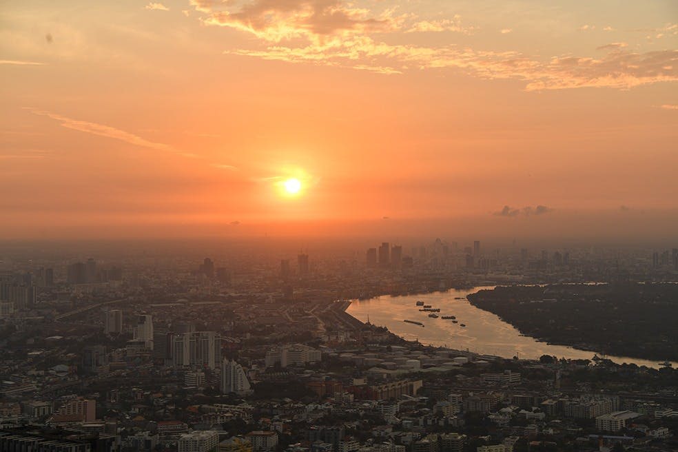 주황색 하늘, 눈에 띄는 강, 아래에 흩어져 있는 건물과 구조물이 있는 석양의 도시 풍경.