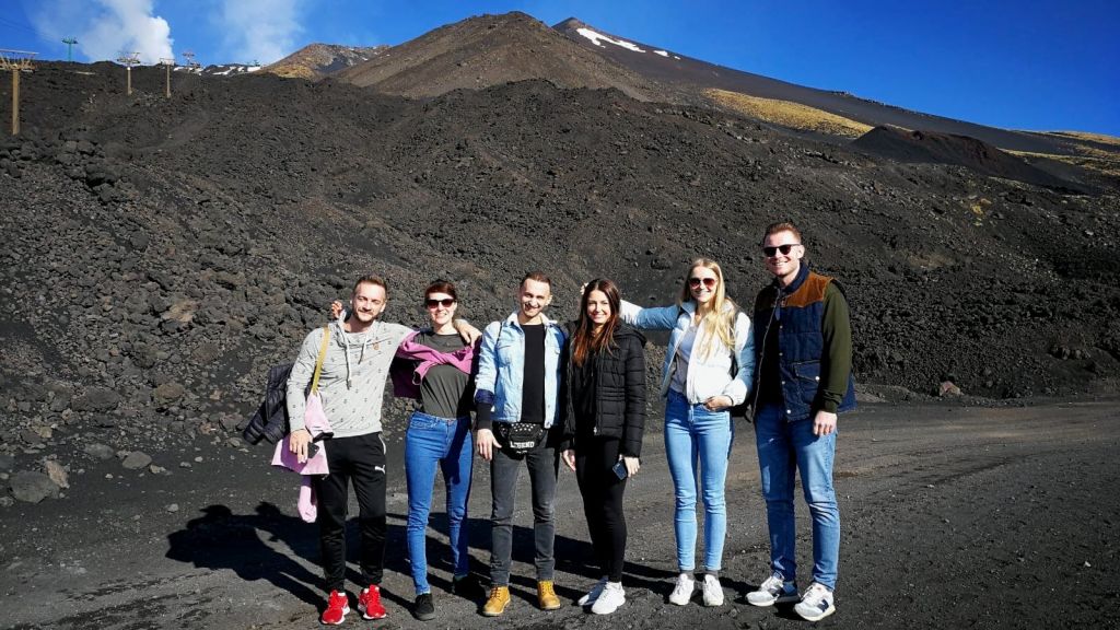 산과 희박한 설원을 배경으로 바위투성이의 화산 지대 앞에 5명의 사람들이 서 있습니다.