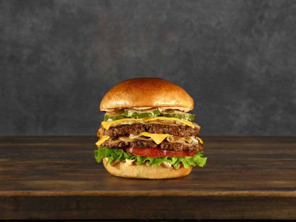 짙은 질감의 배경이 있는 나무 표면에 양상추, 토마토, 피클, 소스가 들어간 더블 치즈버거입니다.