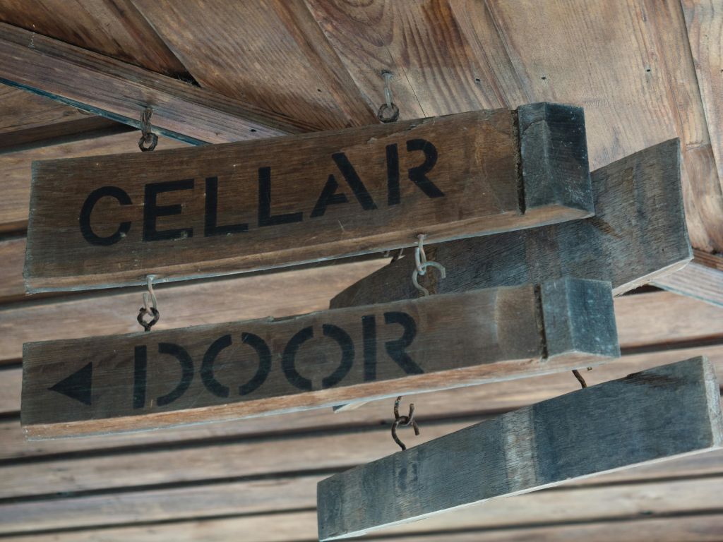 검은색으로 칠해진 "지하실" 과 "문" 이라는 문구가 있는 나무 천장 아래에 나무 표지판을 걸고 있습니다.