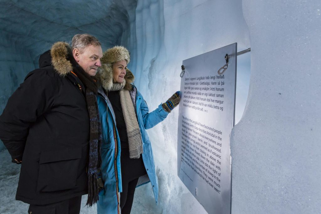 겨울 옷을 입은 두 사람이 얼음 동굴 안에서 표지판을 읽고 있습니다. 벽과 바닥은 얼음으로 되어 있습니다.