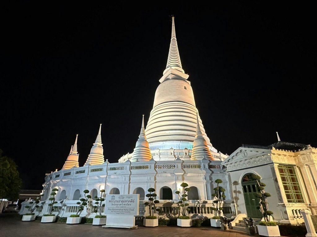 어두운 밤하늘을 배경으로 여러 개의 작은 탑과 녹지가 있는 조명이 밝은 흰색 스투파입니다.
