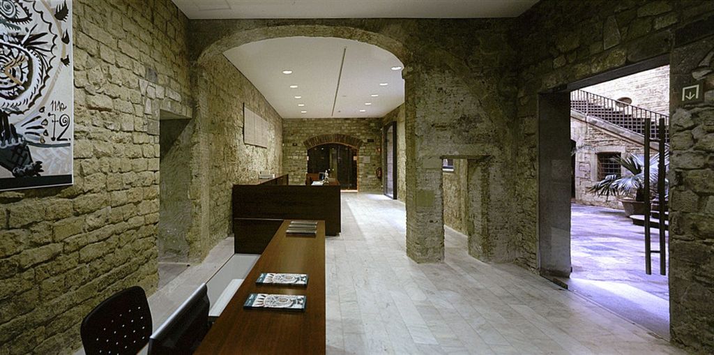 오목한 조명이 있는 아치형 천장 아래, 카운터에 돌담, 나무 책상, 책자가 있는 현대적인 사무실입니다.