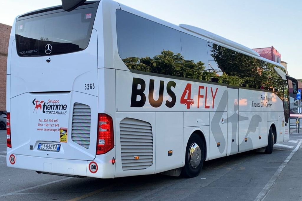 "bus 4 FLY" 표지판이 있는 흰색 버스가 거리에 주차되어 있으며, 창문에 나무가 반사되어 있습니다.