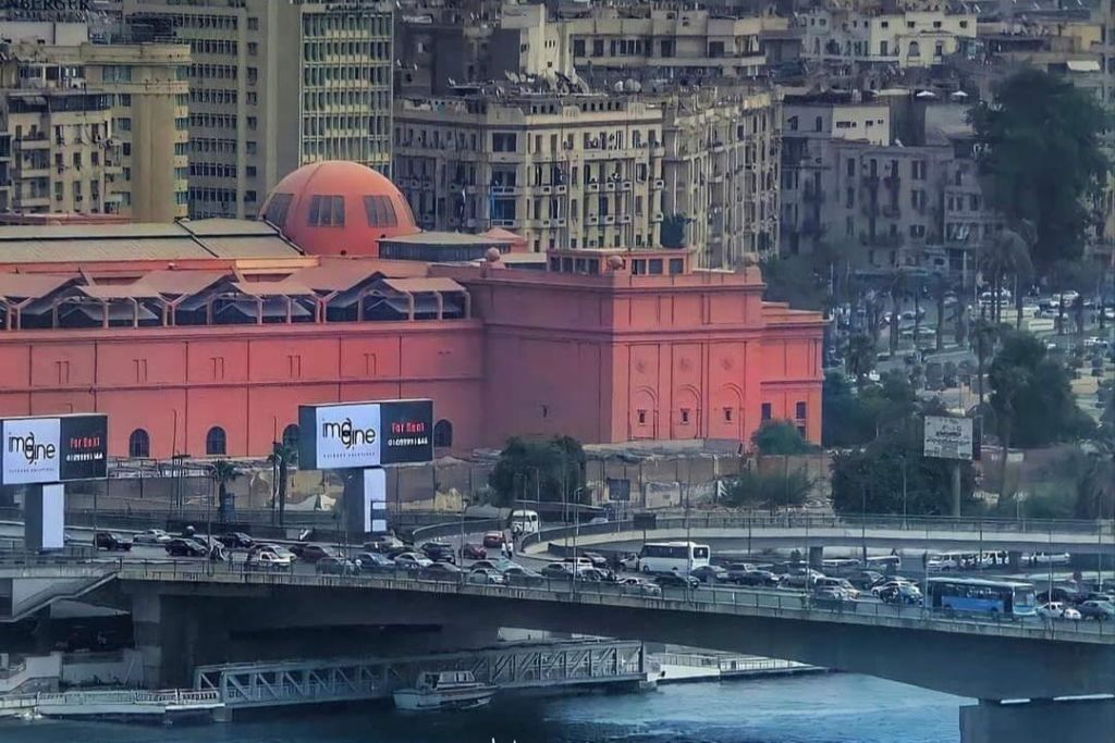 교통 체증이 심하고 높은 베이지색 건물을 배경으로 한 도심의 대형 오렌지색 건물과 붐비는 다리.