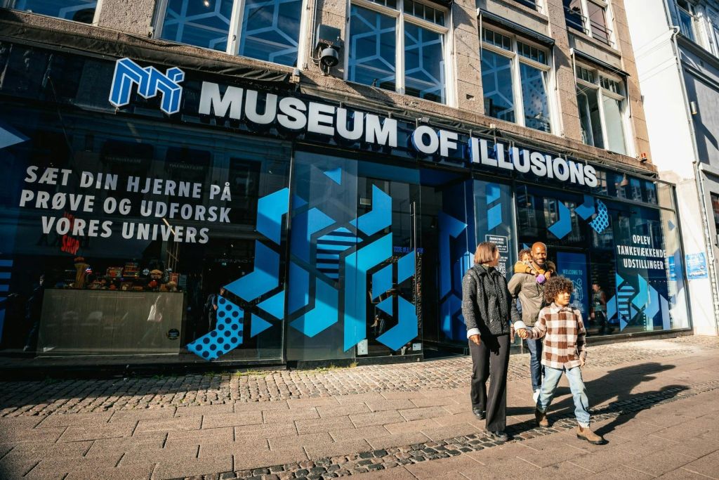 현대적인 파란색 기하학적 디자인과 대형 상점 간판이 있는 환상 박물관을 지나가는 가족.