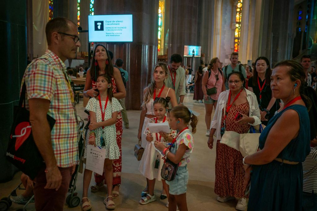 어린이와 성인을 포함한 한 무리의 사람들이 스테인드글라스 창문이 있는 건물 안에 서서 목에 빨간 방아끈을 두르고 있습니다.