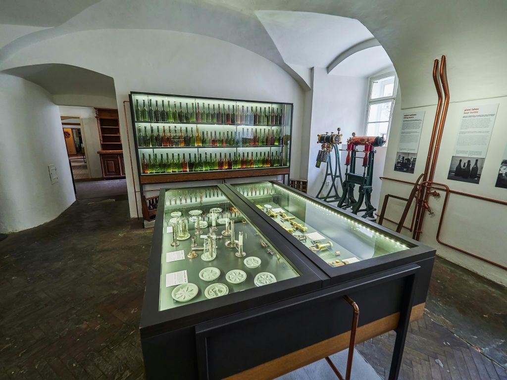 역사적인 도구, 기계 및 흰색 벽에 다채로운 병 선반이 있는 유리 케이스가 있는 박물관 전시실입니다.