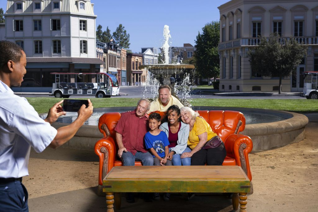 한 남성이 분수대 앞 주황색 소파에 앉아 건물들을 배경으로 사진을 찍고 있습니다.