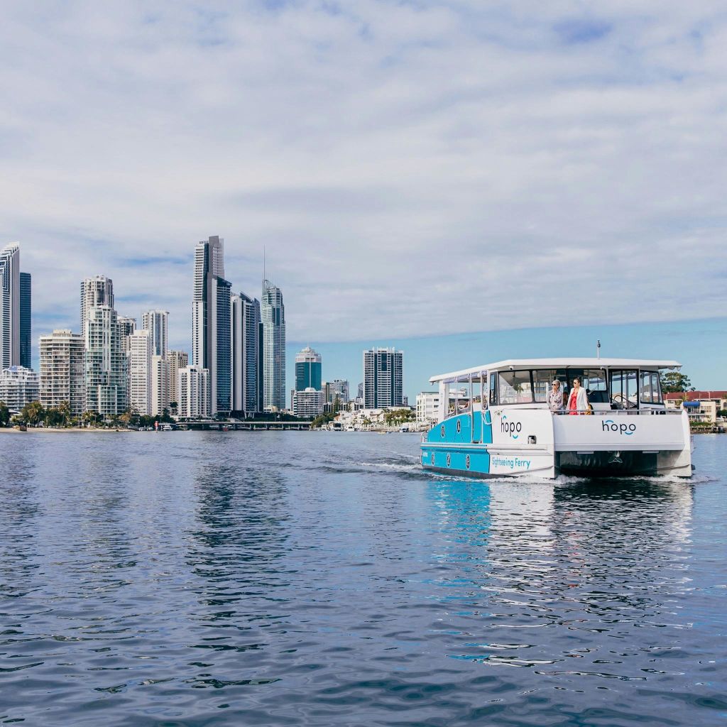 높은 건물의 도시 스카이라인과 푸른 하늘을 배경으로 사람들이 탑승한 페리가 잔잔한 바다를 가로질러 이동합니다.