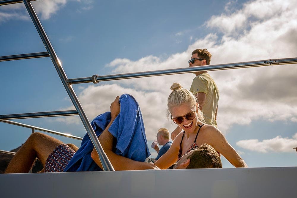 선글라스를 쓴 여성이 미소를 짓고, 선글라스를 쓴 남성이 서 있으며, 다른 남성은 파란 수건을 들고 누워 있습니다.