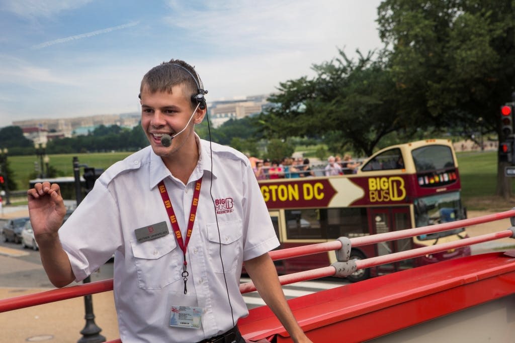 헤드셋이 달린 흰색 유니폼을 입은 남성이 워싱턴 D.C. 의 투어 버스에 서서 제스처를 취하고 있습니다.
