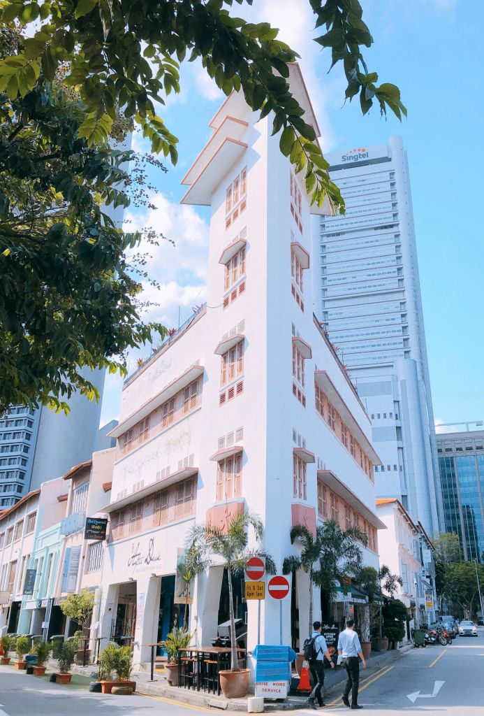 녹지와 높은 건물로 둘러싸인 분홍색 창문으로 포인트를 준 높고 좁은 흰색 건물.