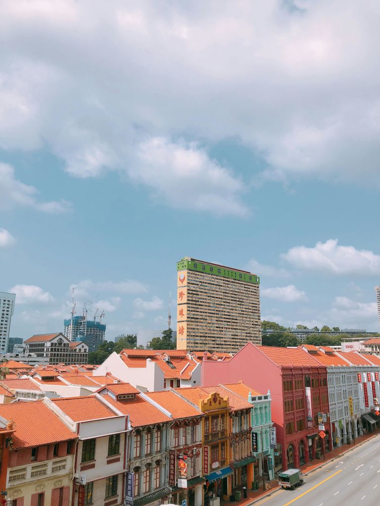 붉은 기와 지붕이 있는 화려한 건물과 높은 직사각형 건물을 배경으로 한 도시 풍경.