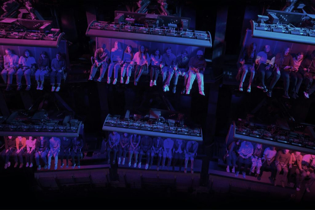 보라색과 파란색 조명이 있는 어둡고 밝은 환경에서 여러 층으로 이루어진 놀이 기구에 앉아 있는 사람들.