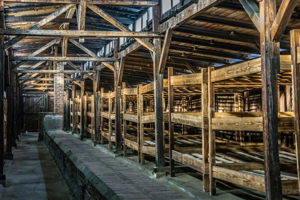 나무 대들보와 벽돌 바닥이 있는 조명이 희미하고 소박한 건물 내부에 여러 층의 이층 침대가 있는 목조 구조물입니다.