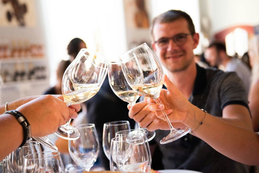 안경을 쓴 한 남성이 사교 모임에서 다른 사람들과 와인잔을 움켜쥐고 미소를 지으며 카메라를 바라보고 있습니다.