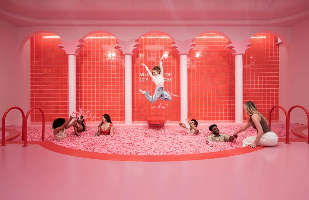 아이스크림 박물관의 분홍색 스프링클이 가득한 수영장에서 노는 사람들. 한 사람이 중앙에서 공중으로 점프하고 있습니다.