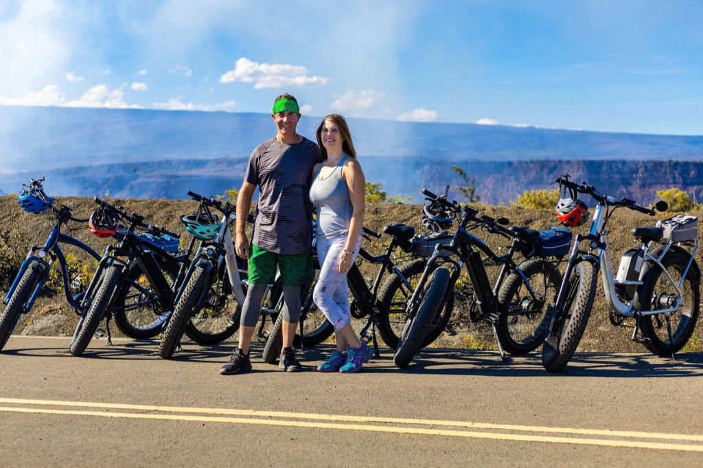 운동복을 입은 두 사람이 아름다운 산을 배경으로 자전거 옆에 서서 미소를 짓고 있습니다.