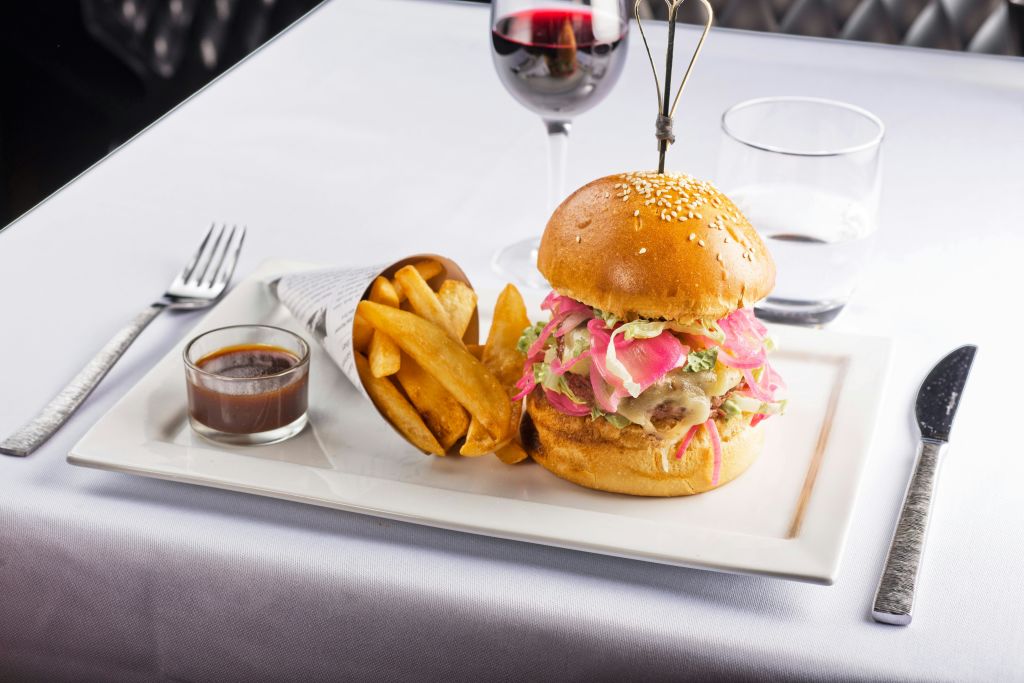 양파 절임, 감자튀김을 종이 콘에 넣고 흰 식탁보에 적포도주 한 잔을 곁들인 고급 햄버거.